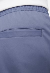 Siniset kangashousut, joissa on sileä pinta, joustava vyötärö ja yksi takatasku siistillä sauman viimeistelyllä.