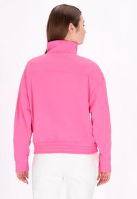 Pullover in pile a mezza zip di un vivace colore rosa, con colletto alto e orlo a coste. Maniche lunghe con polsini regolabili per il massimo comfort.