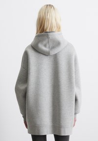 Hanorac gri supradimensionat, cu o textură netedă, glugă cu șnur, umeri căzuți și manșete cu nervuri. Design simplu, fără modele sau accente vizibile.
