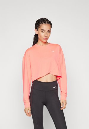 Cropped, long-sleeve athletic top in bright coral with a rounded neckline and layered front design, paired with high-waisted black leggings.