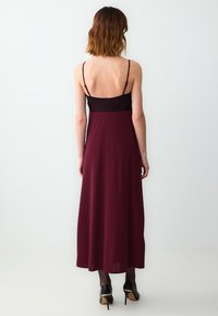 Burgundowa maxi sukienka z dopasowanym koronkowym gorsetem, cienkimi ramiączkami i luźną spódnicą, charakteryzująca się gładką fakturą i jednolitym kolorem.