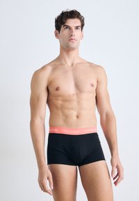 Zwarte boxershorts met een roze Calvin Klein logo tailleband; zachte textuur; aansluitend ontwerp; gedragen door een shirtloze mannelijke model.