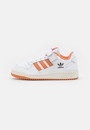 Hvid Adidas lav sneaker med orange striber, orange inderfor, Velcro rem og beige sål med orange mønster.