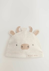 Gorra de algodón beige con diseño de vaca que incluye orejas y pequeños cuernos, una cara impresa y el texto "mini moo" en marrón claro.
