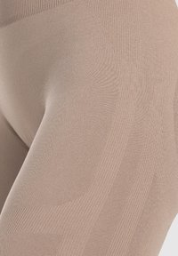 Beige legging gemaakt van gebreide stof met textuur en geribbelde details, met een soepele tailleband en contournaadpatronen.