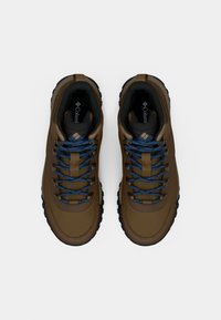 Brown outdoor shoes with textured fabric, black rubber soles, blue laces, and reinforced toe caps. Logo visible on the tongue.