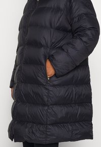 Steppjacke in dunkelblau mit gestepptem Muster, Reißverschlusstaschen und hohem Kragen. Das Material scheint glänzend und wasserabweisend zu sein.