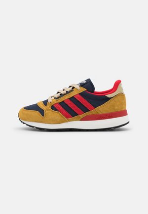 Scarpa da uomo Adidas con mesh blu navy, sovrapposizioni in suede color senape, strisce rosse, lacci beige e suola bianca, vista laterale.