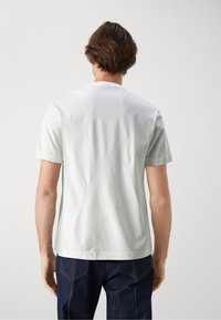 Weißes Baumwoll-T-Shirt, kurze Ärmel, Rundhalsausschnitt, glatte Textur, schlichtes Design, getragen mit dunkelblauen Jeans, von hinten betrachtet.