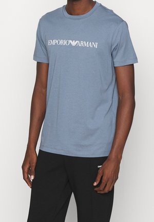 Jasnoniebieska bawełniana koszulka z krótkimi rękawami, okrągłym dekoltem i białym logo "EMPORIO ARMANI" na wysokości klatki piersiowej. Prosty, luźny krój.