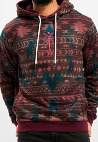 Sudadera con capucha de base marrón, con patrones tribales en azul y rosa. Incluye un gráfico de palmera y cordones blancos.