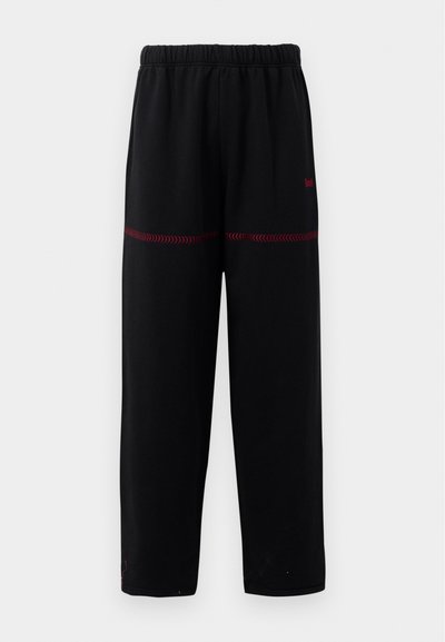 Čierne nohavice s voľným strihom, ktoré majú mäkkú textúru, elastický pás a červené švy zdobí dolné panely a logo.