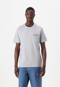 Pilkos spalvos apvalaus kaklo marškiniai, pagaminti iš medvilnės, su mažu raudonu ir mėlynu "HILFIGER" logotipu ant krūtinės kišenės. Trumpomis rankovėmis, laisvo kirpimo.