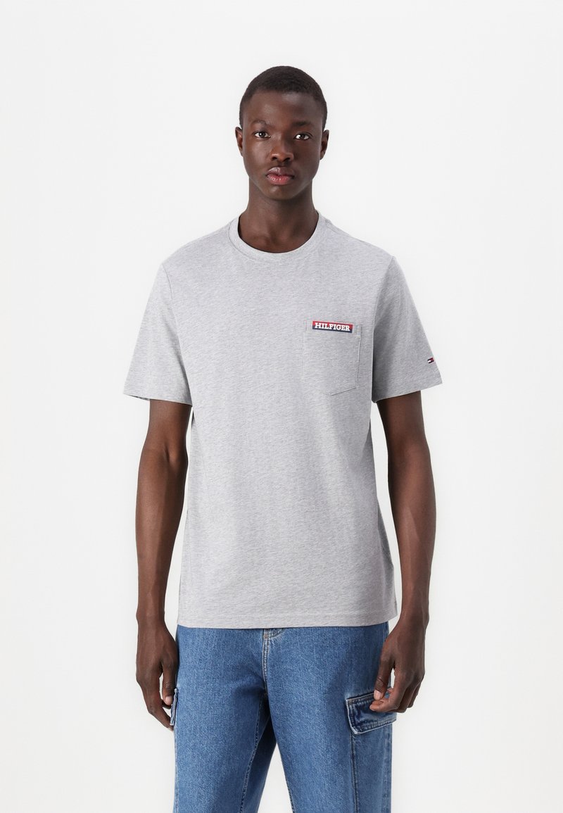 Pilkos spalvos apvalaus kaklo marškiniai, pagaminti iš medvilnės, su mažu raudonu ir mėlynu "HILFIGER" logotipu ant krūtinės kišenės. Trumpomis rankovėmis, laisvo kirpimo.