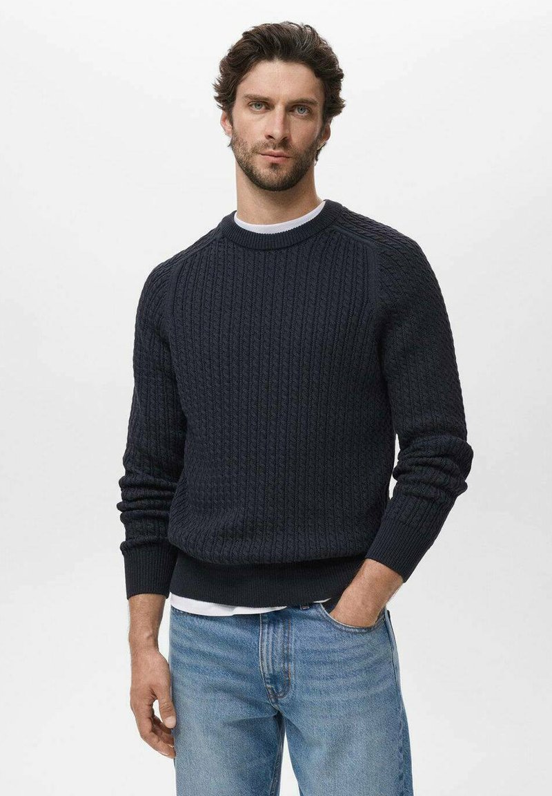 Suéter de punto acanalado en azul marino oscuro con cuello redondo, patrón texturizado y puños ajustados, combinado con jeans de color azul claro. Diseño simple y clásico.