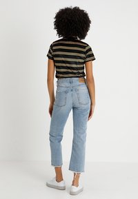 Camiseta a rayas en negro y amarillo, vaqueros de denim azul claro con dobladillo recortado y zapatillas blancas con suela texturizada.