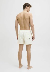 Costumi da bagno leggeri gialli chiari da uomo con vita elastica, tasca posteriore a toppa e cuciture piatte, mostrati da dietro.