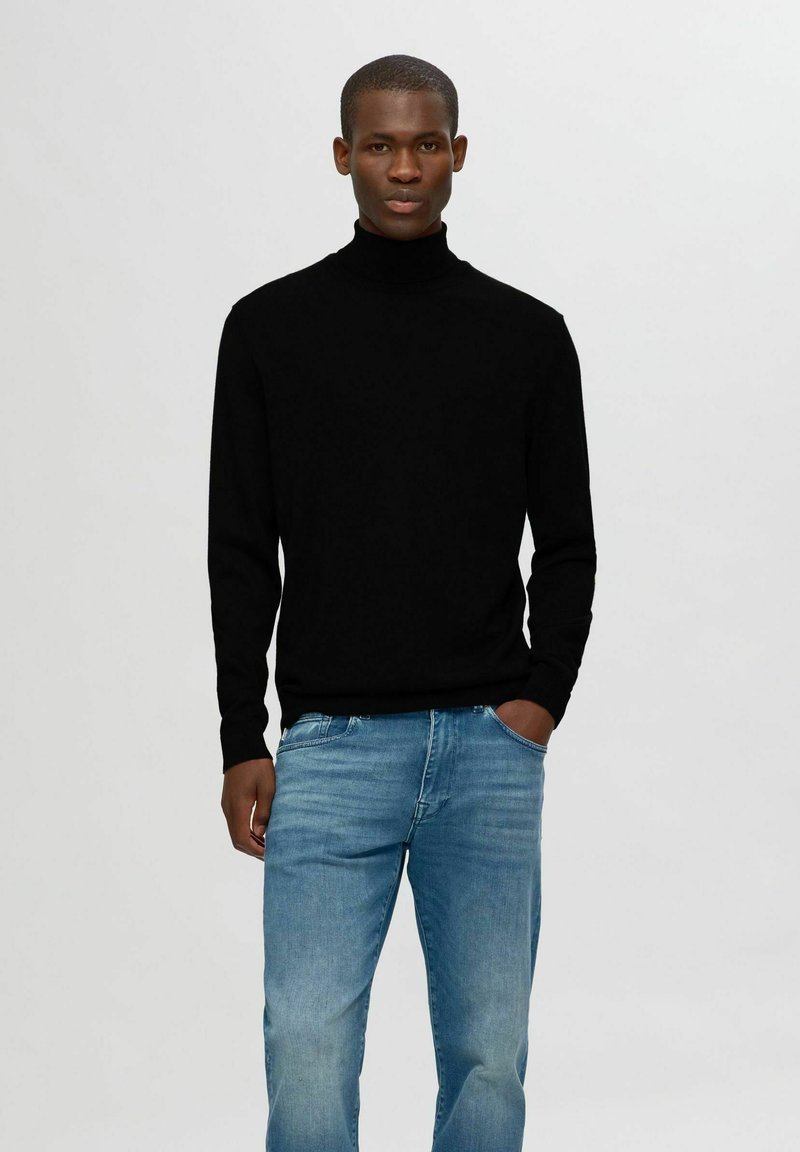 Svart turtleneck-tröja i mjukt material, kombinerad med ljusblå jeans. Passformen är avslappnad med långa ärmar och ribbat avslut.
