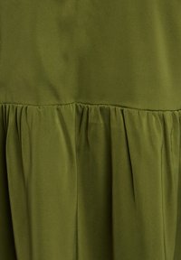 Žalias audinys su lygiu paviršiumi, išpjaustytomis klosčių detalėmis palei apatinį kraštą. Medžiaga yra lengva ir turi švelnų apdailą.