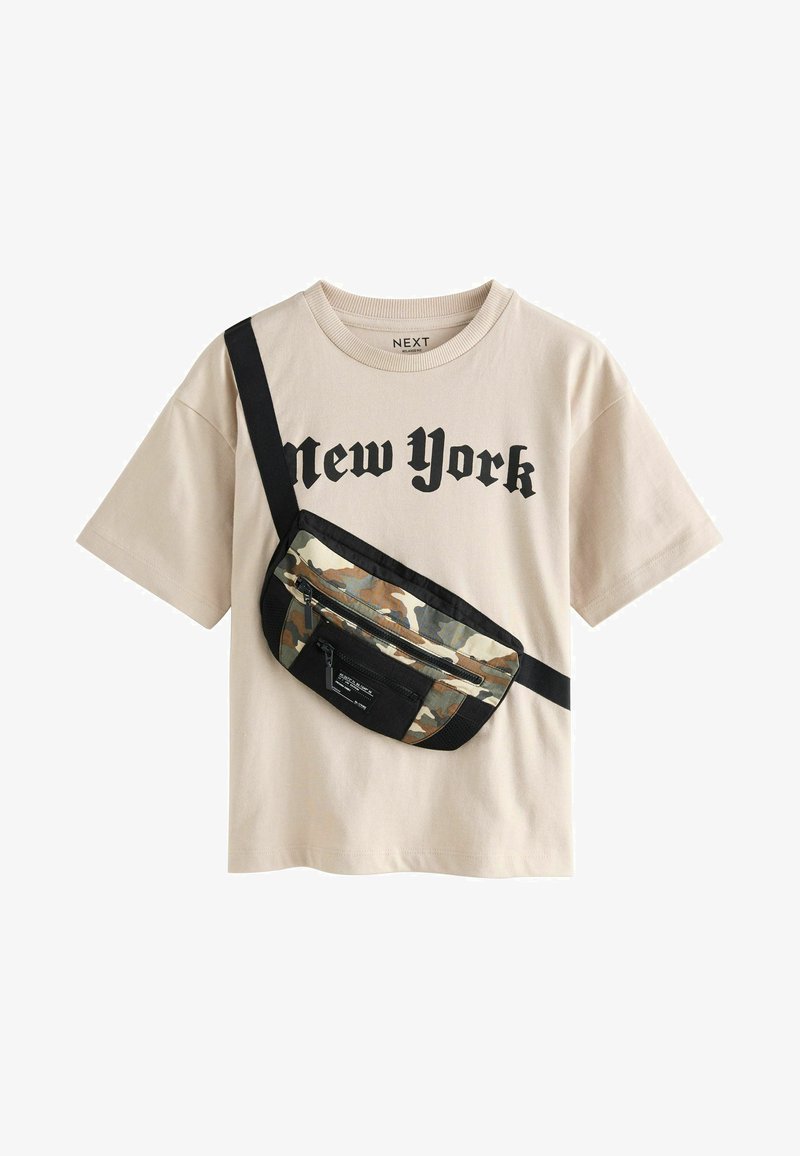 Beżowy t-shirt z czarnym napisem "New York" oraz torba na ramię w kamuflażowym wzorze, z czarnymi paskami i zamkami błyskawicznymi z przodu.