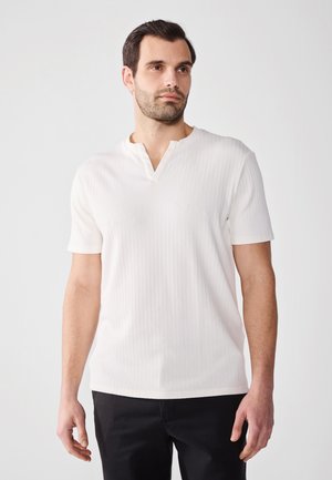Chemise blanche à manches courtes côtelée avec un col en V, présente un tissu texturé et une coupe ajustée, associée à un pantalon noir.