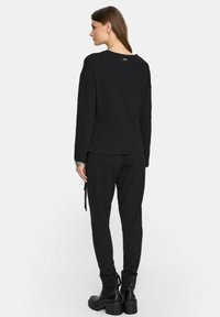 Czarny longsleeve z okrągłym dekoltem, dopasowany do zwężających się czarnych spodni, z elastycznymi mankietami i wiązaniem w talii.