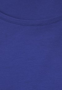 Kungligt blått tyg med en mjuk, räfflad struktur. Den runda halsringningen har en ren sömnadsfinish som framhäver den jämna, livfulla färgen.