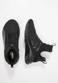 Mustat Puma-loafersit verkko-yläosalla, elastisilla nauhoilla ja pehmustetuilla pohjilla valkoista taustaa vasten.