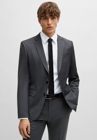 Grijze suit met een gestructureerde afwerking, twee knopen, notch revers, gecombineerd met een wit shirt en een zwarte stropdas. Slim fit ontwerp.