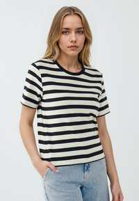 T-shirt a maniche corte a righe nere e crema, con scollatura rotonda, realizzata in un materiale morbido, abbinata a jeans di denim azzurri chiari.