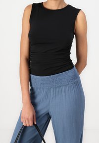 Svart ärmlös topp med rynkad textur, matchad med ljusblå byxor med elastisk midja i skrynklig tyg. Håller en svart handväska.