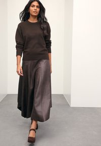 Brown knitted sweater and a long, flowing dark brown leather skirt, paired with brown platform shoes. Smooth texture and relaxed fit.