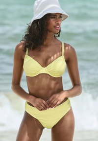 Geel geribbeld bikini set met een gestructureerde top met verstelbare banden en bijpassende high-waisted onderkant, tentoongesteld op een strand.
