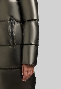 Vyteplená parka z lesklého tmavozeleného materiálu, so zipsovým vreckom na rukáve, s nadýchanou textúrou a čistým strihom.