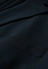 Tissu bleu marine foncé avec de fines rayures verticales et une couture visible, montrant une partie d'une poche et un bord plié.