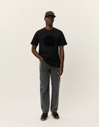 Čierne tričko s krátkym rukávom s kruhovou grafickou potlačou. Spárované so sivými nohavicami s rovnými nohavicami a čiernymi topánkami. Čiapka má kockovaný vzor.