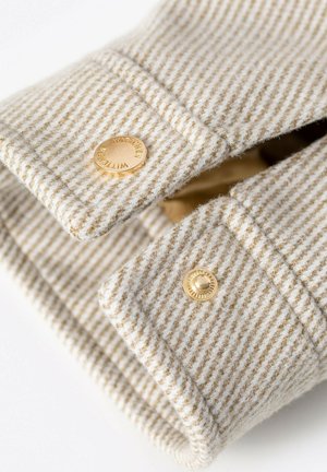 Beige met witte gestreepte stof met goudkleurige knopen. Close-up van een overhemdbies, met nadruk op textuur en naaibewerkingen.