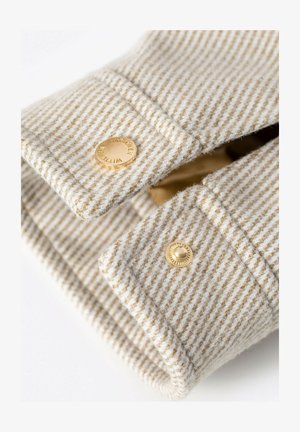 Beige met witte gestreepte stof met goudkleurige knopen. Close-up van een overhemdbies, met nadruk op textuur en naaibewerkingen.