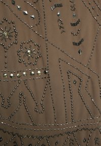 Gyöngyözött textil bonyolult ezüst gyöngy- és flitterdíszítéssel, bézs alapon, geometriai mintákkal és változatos textúrákkal.