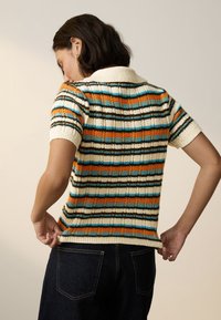 Pletený polo svetr s krátkými rukávy, zdobený vícenásobnými pruhy v oranžové, modré, černé a krémové barvě, s žebrovaným límcem a lemem.