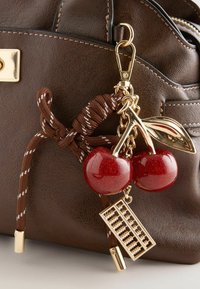 Bruine leren handtas met een bevestigde sleutelhanger met glinsterende rode kersen, gouden blad, abacus charm en bruine gestreepte koord.