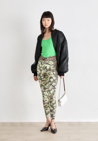 Zwarte leren bomberjack over een heldergroen tanktop, gecombineerd met patroonleggings met bloemen en luipaardprint, en zwarte ballerina's.