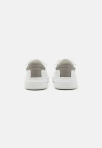 White leather sneakers with a light gray accent on the heel, featuring a smooth texture and a padded collar, branded with Calvin Klein.