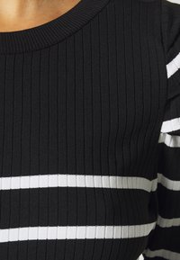 Schwarzer gerippter Pullover mit weißen horizontalen Streifen, einem runden Ausschnitt und strukturiertem Stoff. Fokus auf dem vertikalen Rippenmuster.