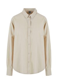 Chemise beige à manches longues avec col pointu et boutons visibles sur le devant, présentée sur fond blanc.