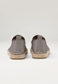Espadrilles de tela con un patrón a cuadros en azul y marrón, suelas de cuerda de yute y forro de tela marrón. Con tiradores en la parte trasera para facilitar su uso.