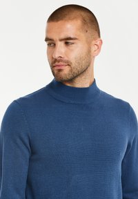 Blauer, gestrickter Rollkragenpullover mit einem gerippten Kragen, langen Ärmeln und einer glatten Textur. Nahaufnahme des Ausschnitts und der Schulter.
