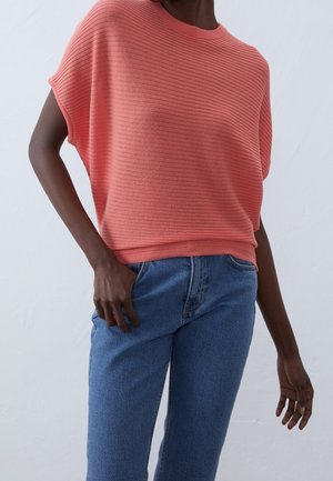Korallefarbenes geripptes Strickoberteil mit lockerer Passform und kurzen Dolmanärmeln, kombiniert mit hochgeschnittenen blauen Jeans. Glatte Textur und lässiges Design.