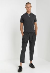 Dunkelgraues Poloshirt mit kurzen Ärmeln, kombiniert mit schwarzen gestreiften Hosen. Schwarze Schnürschuhe. Einfaches und modernes Outfitdesign.