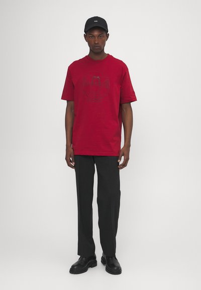 Rotes Baumwoll-T-Shirt mit einem grafischen Druck auf der Vorderseite, kombiniert mit schwarzen Hosen und schwarzen Stiefeln, mit entspannter Passform und kurzen Ärmeln.